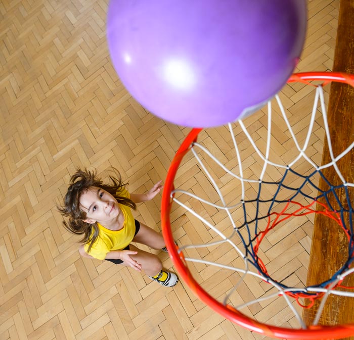 Девочка забрасывает мяч в баскетбольную корзину на уроке физкультуры в детском саду