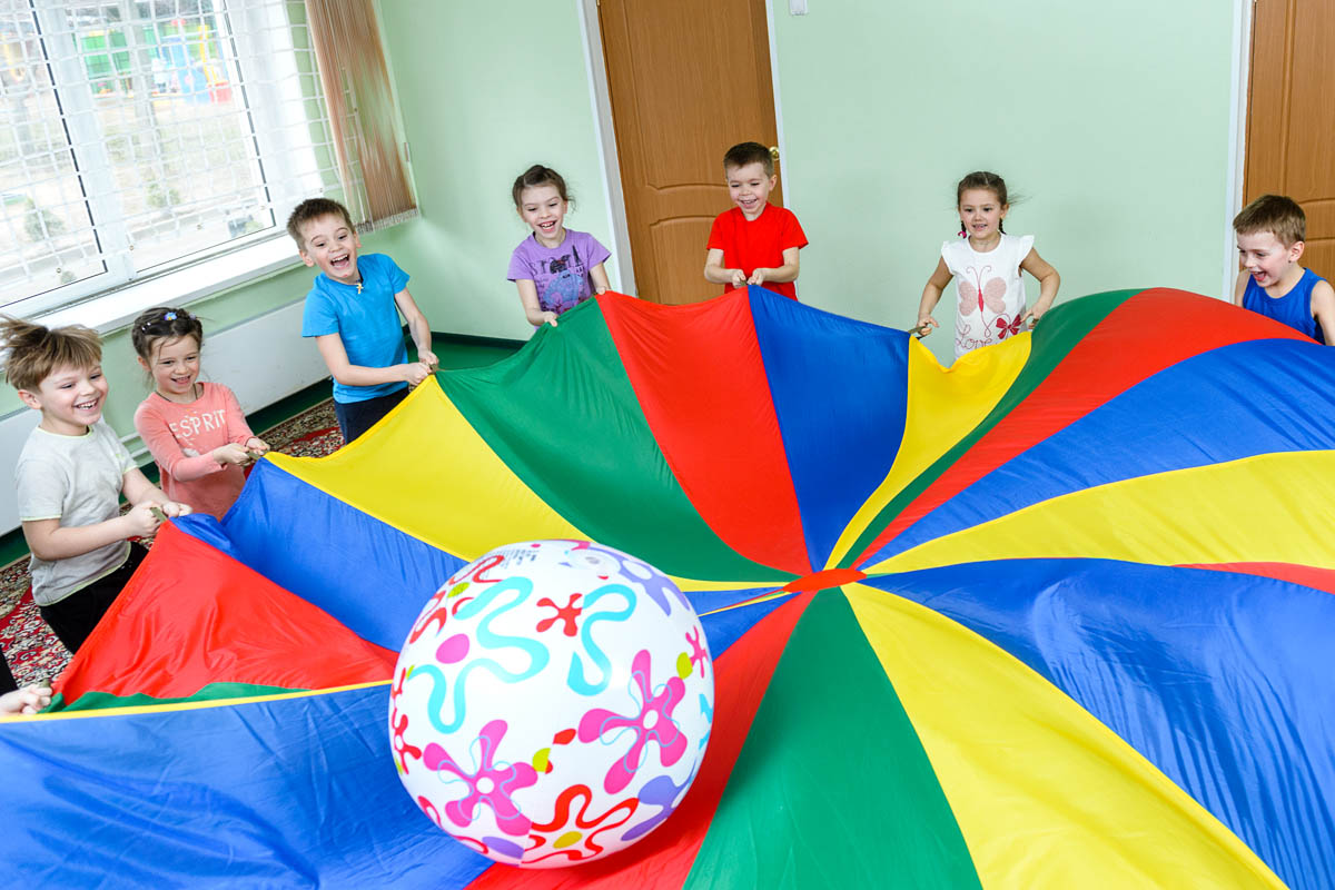 Дети играют на физкультуре в детском саду с парашютом.